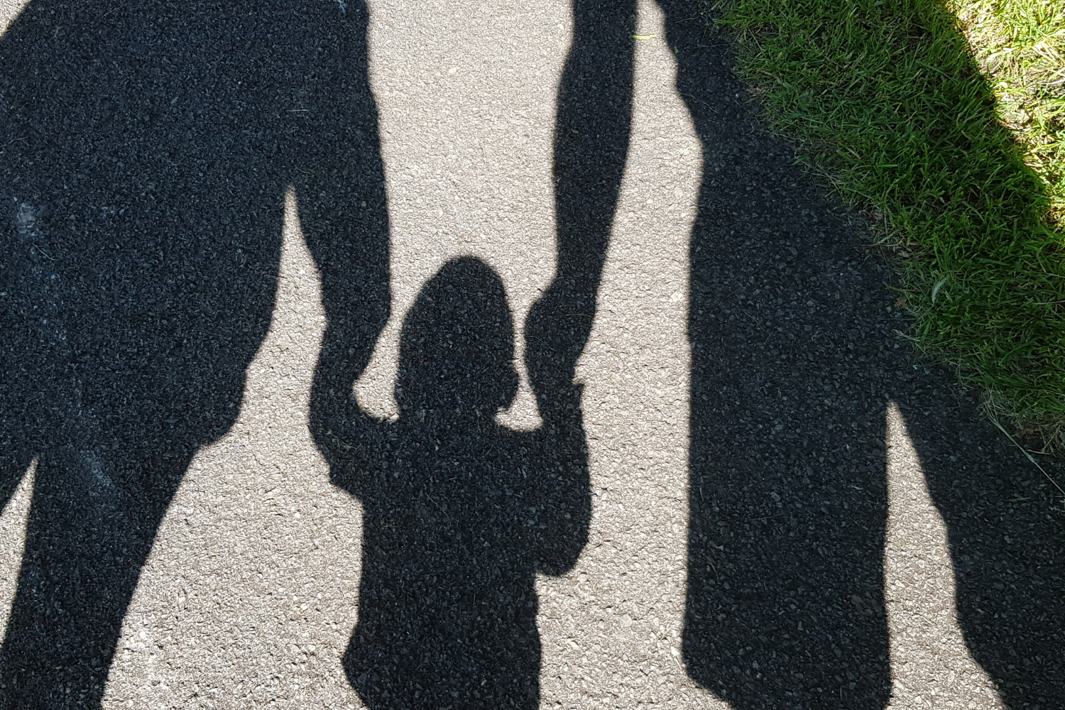 shadows on the ground showing parents holding a childs hands