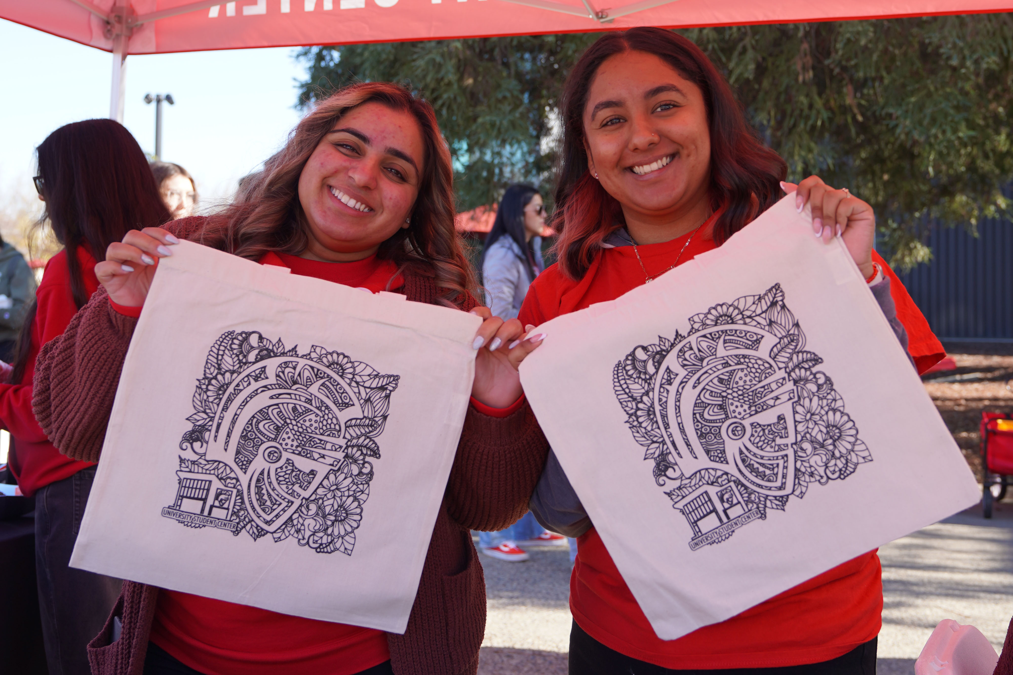 2 students posing with Titus warrior tote bags
