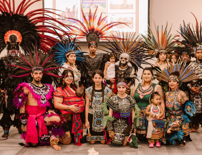 Members of a native tribe dressed in traditional Aztec attire pose in a group photo.