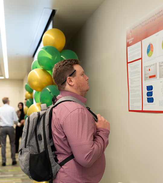 A student reads a research poster at Stan State's 2024 Research, Scholarship and Creative Activity Celebration.