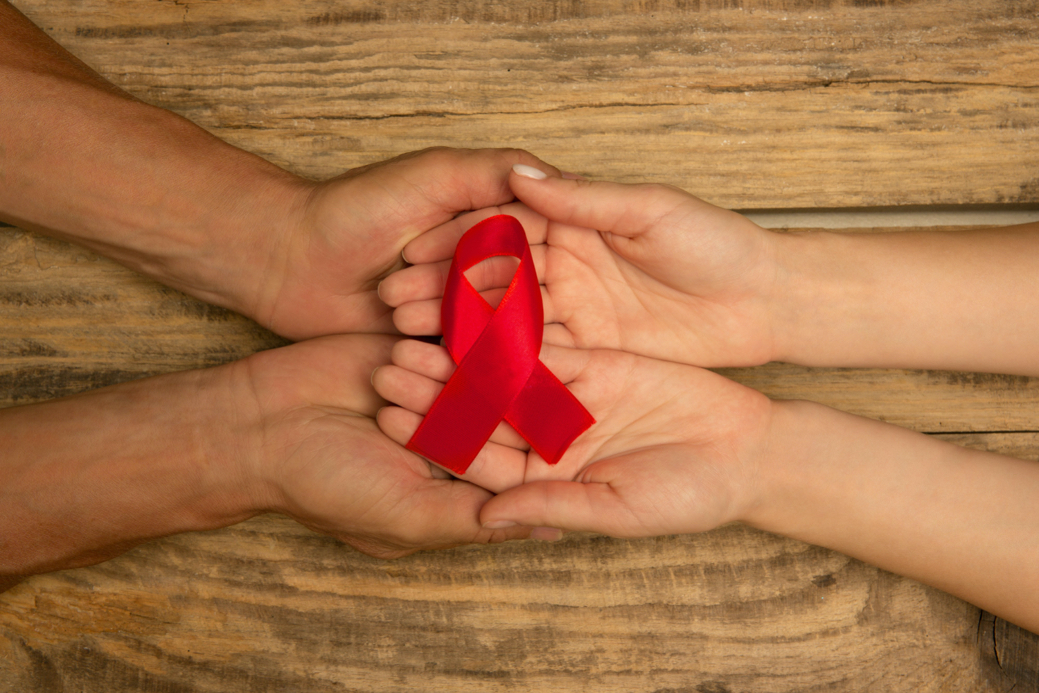 Female and male hands holding red HIV AIDS awareness ribbon.