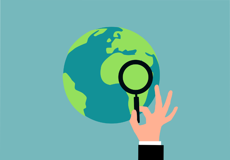 a hand holds a magnifying glass up to a globe