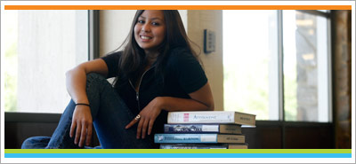Student sitting next to stack of books