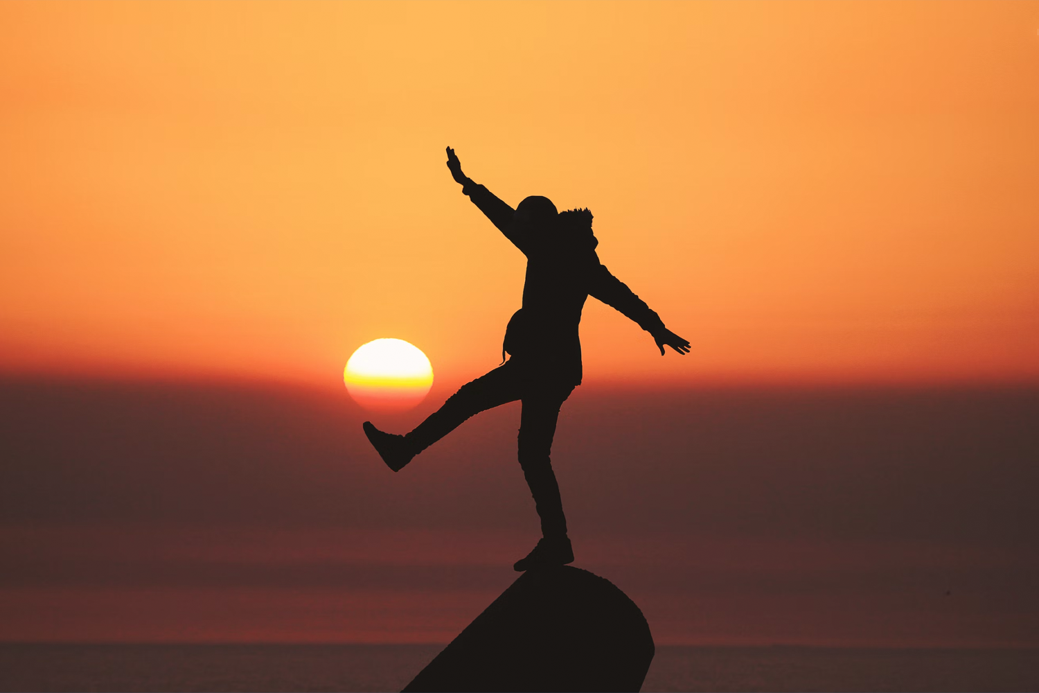 individual's silhouette balancing on a rock during sunset