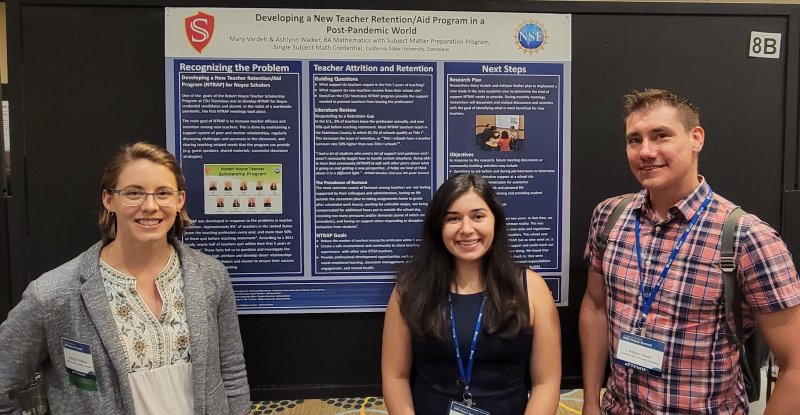 Three people standing in front of an infographic board on a wall