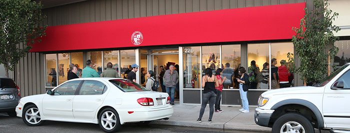 ssas_galleryexterior_01.jpg People standing on sidewalk outside and inside of art gallery near roadway