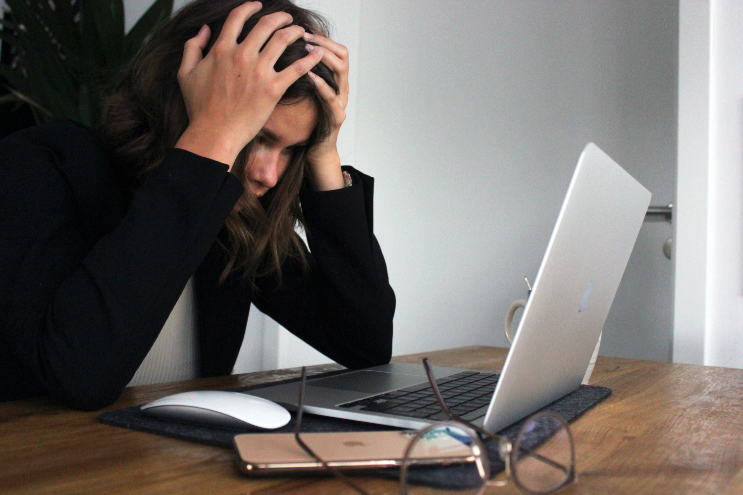 woman in long balck sleeve appearing stressed while staring at a laptop.