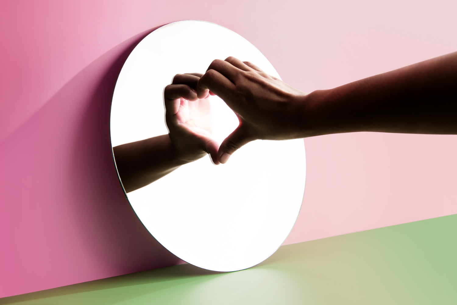a person with one hand to a mirror, creating a heart with the reflection.