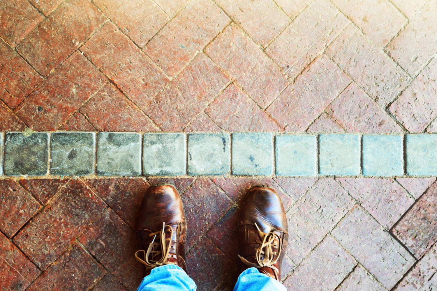 looking down at a pair of feet standing in front of a line in the brick design. 