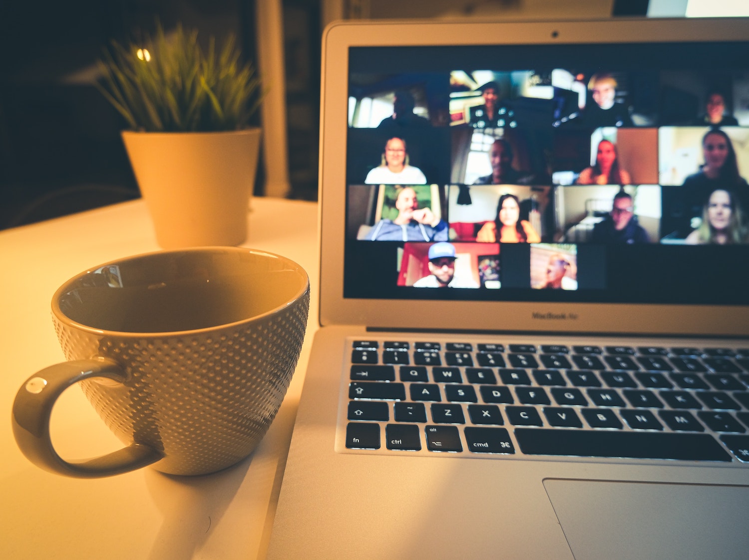 a virtual meeting taking place on a laptop screen with a cup of coffee next to the laptop