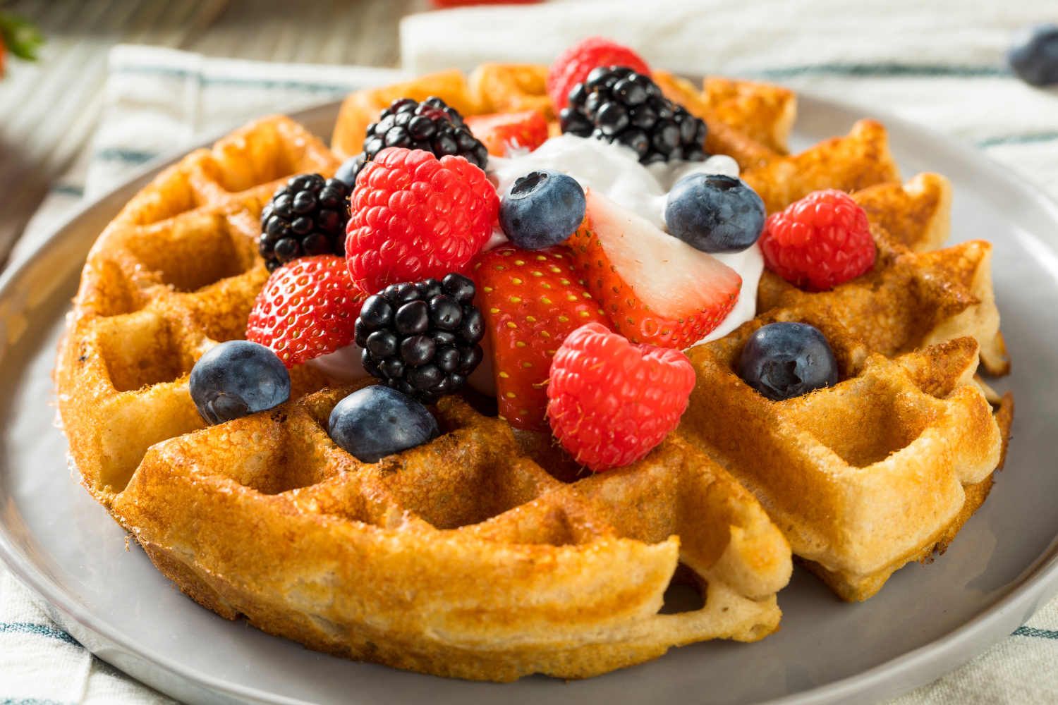 a waffle with fresh strawberries, blackberries and blueberries on top.
