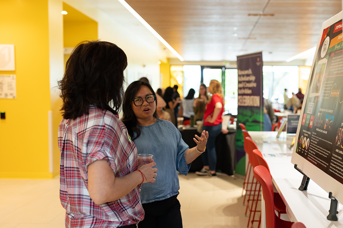 Two women discuss a research poster at the Research, Scholarship and Creative Activity Celebration at Stanislaus State.