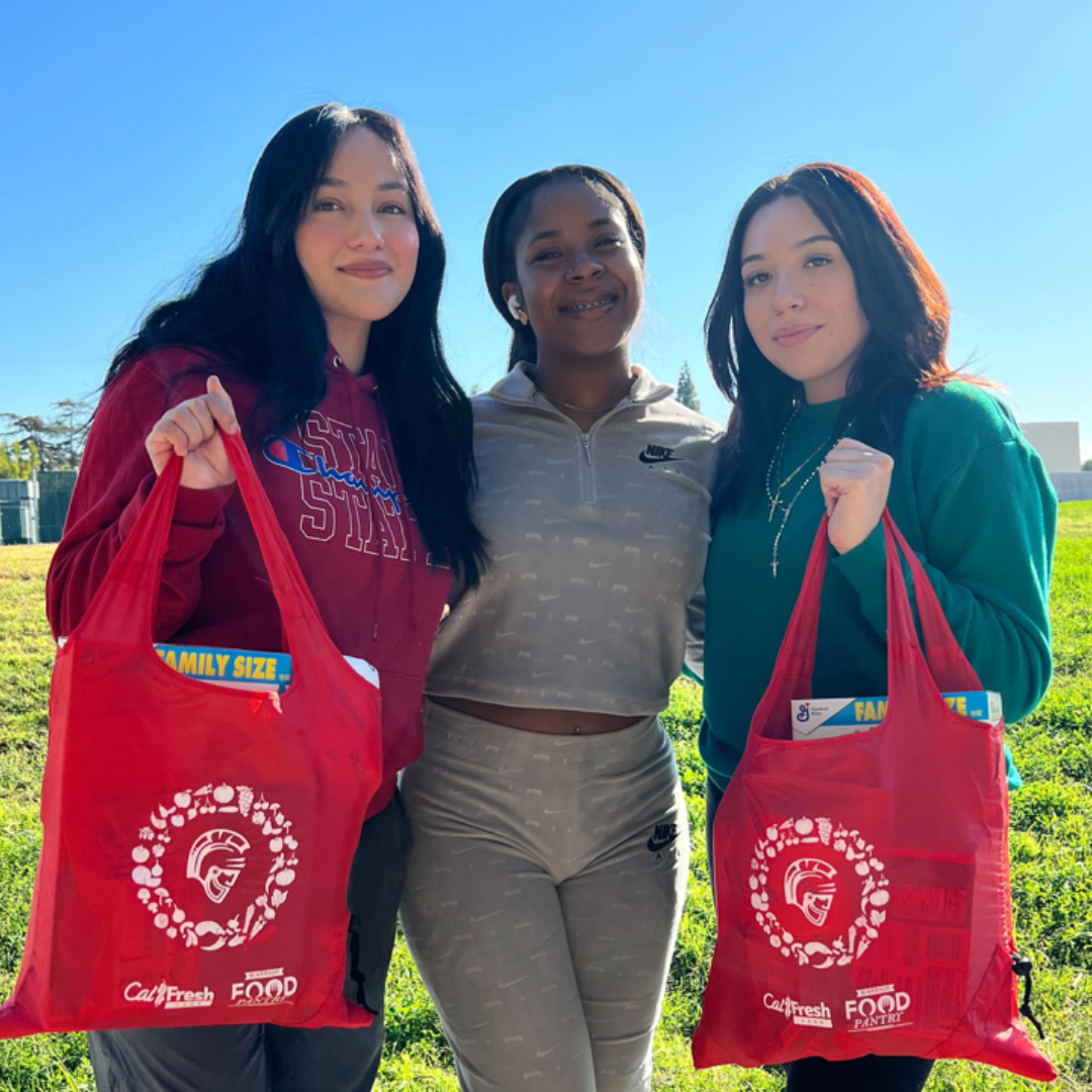 Three students holding a stan state branded bag of groceries.