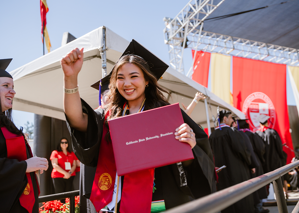 Student celebrating at commencement holding her degree and smiling.