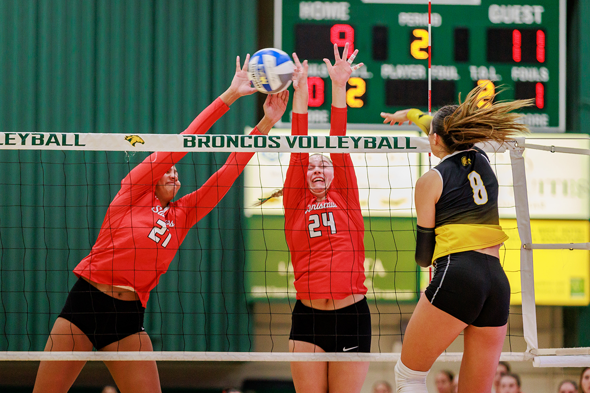 Warriors volleyball players block a shot during a game.