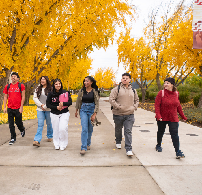 Large group of walking on campus in the fall with trees turning fall colors 