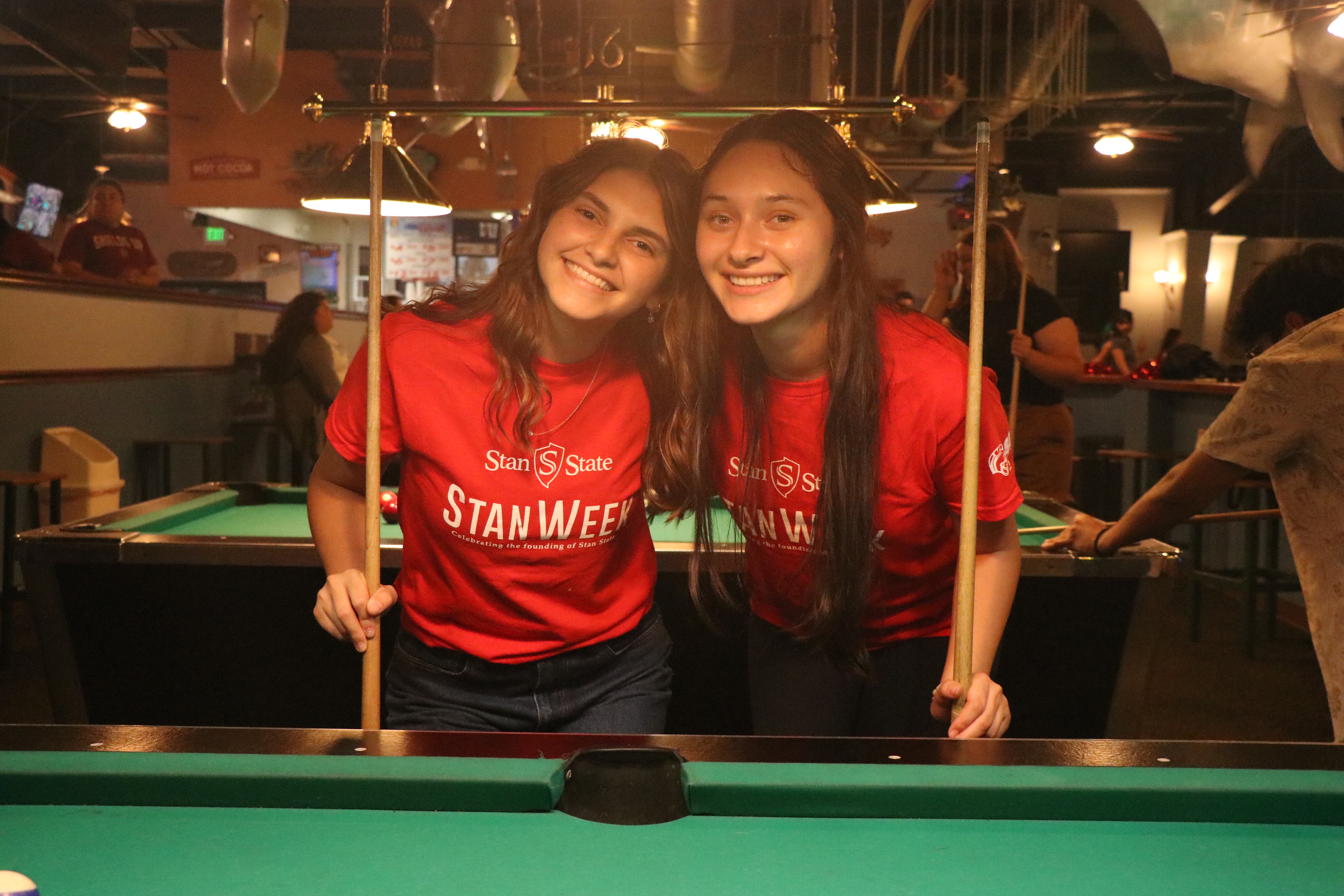 Two students taking picture with pool cues in their hands