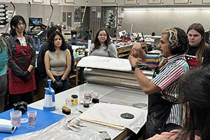 Art students gather around a printmaking demonstration.