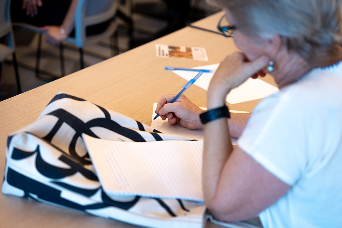 A woman seated at a table is writing on paper.