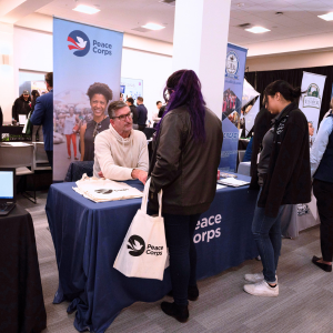 Two students talk to a recruiter at the Peace Corps table at the Career Fair