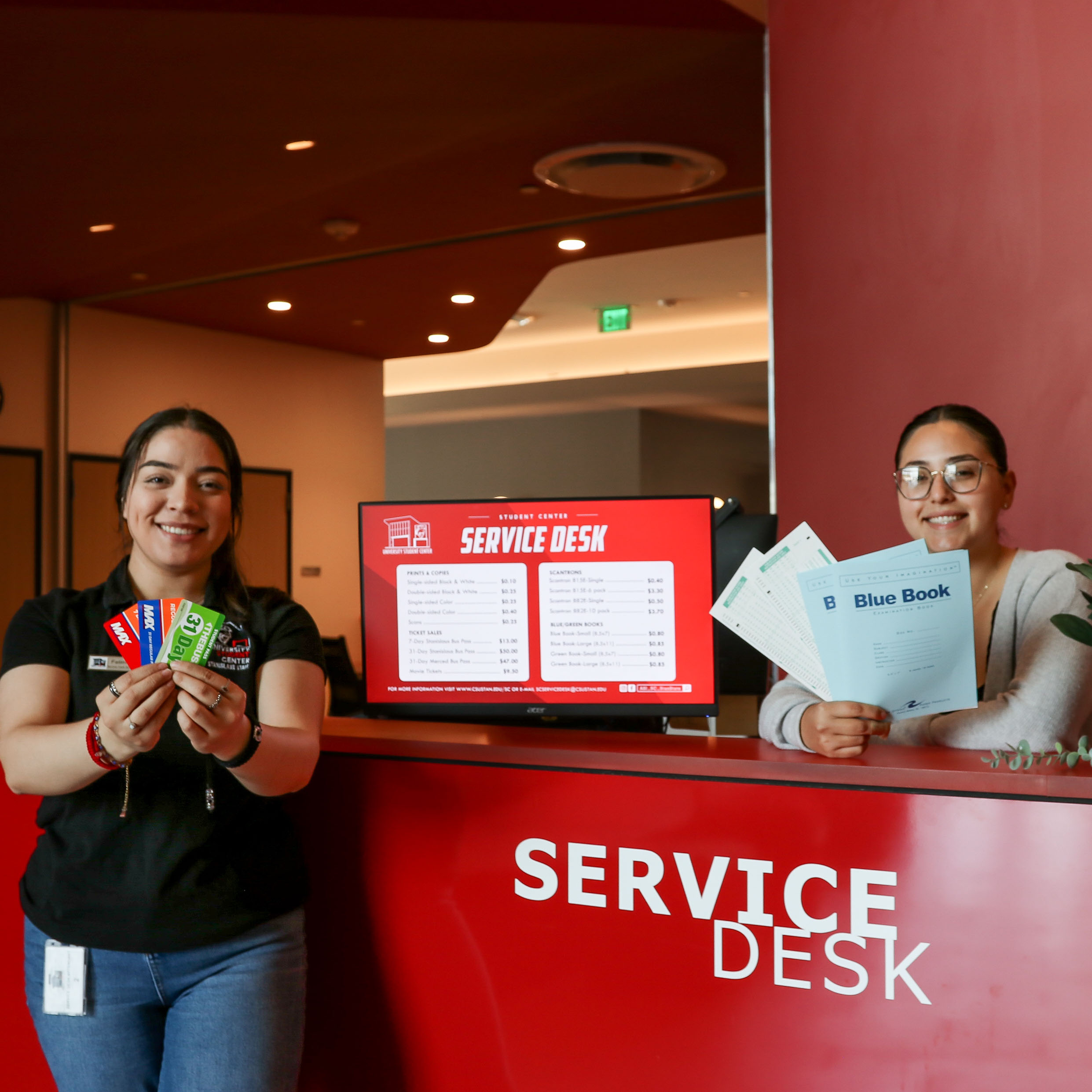 Two students holding out bus passes and blue books