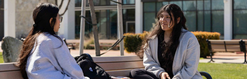 Two students sitting at bench in the quad at Stan State