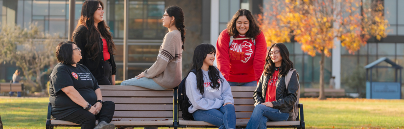 Six students chat near a bench at the quad at Stan State
