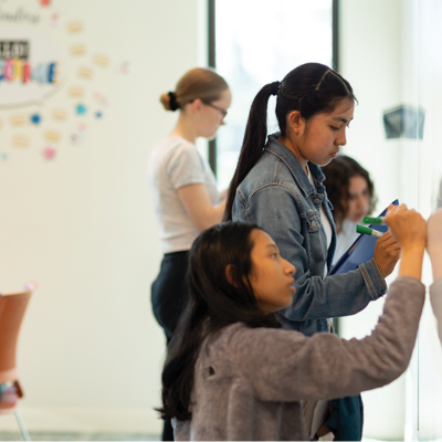 Four students are writing on a whiteboard wall.