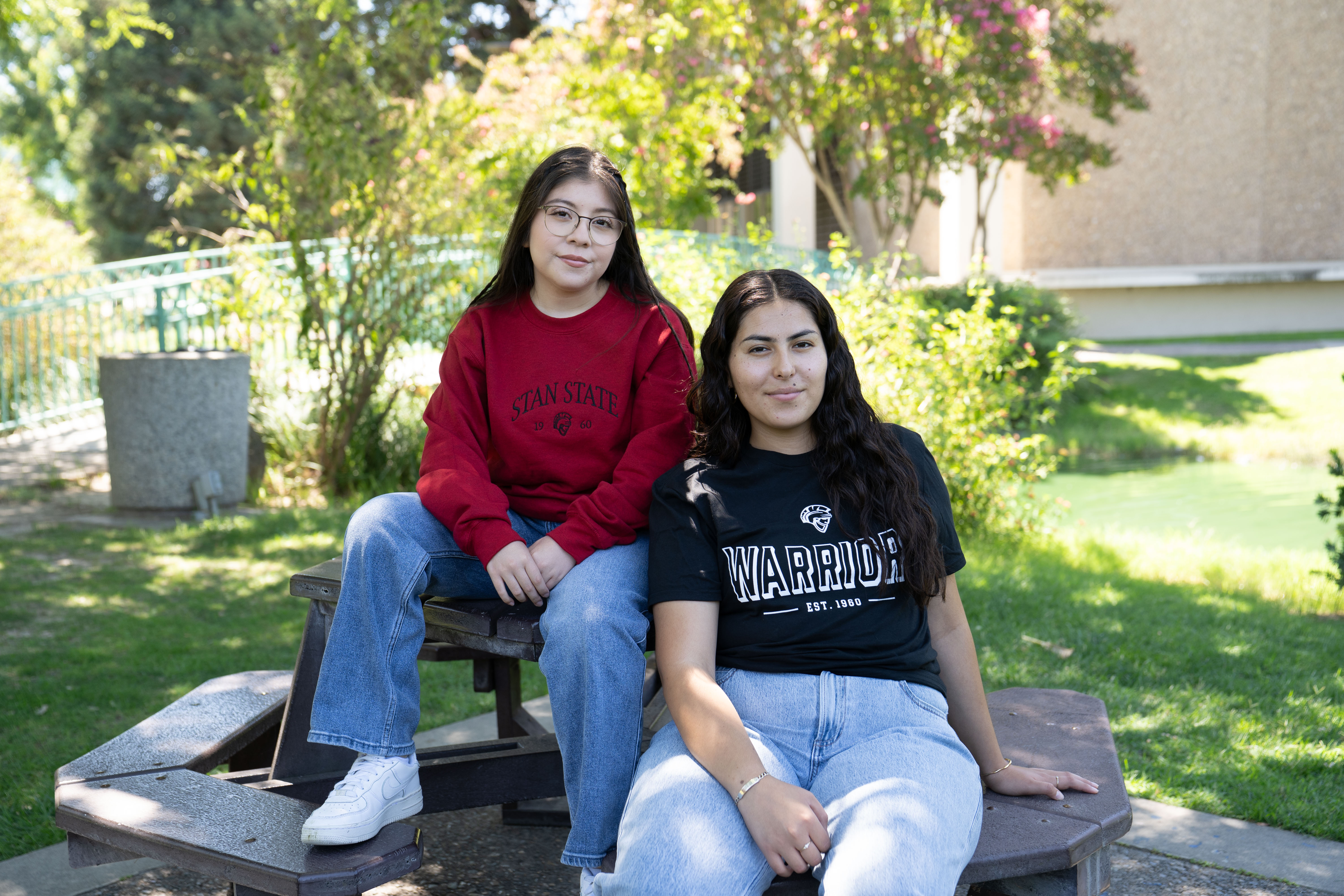 Two students sitting on table wearing new Stan State Merch