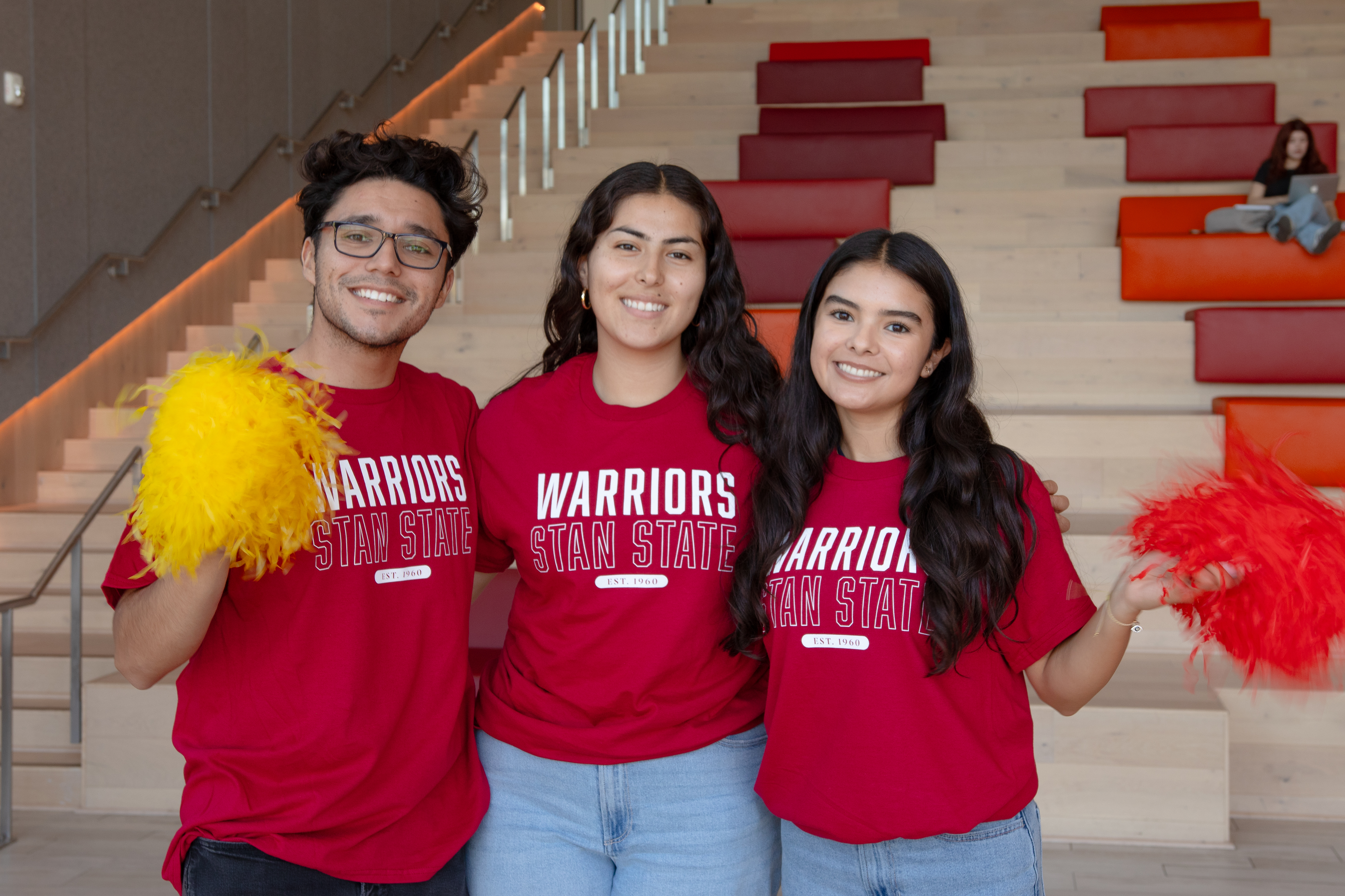 3 students wearing red and posing with pom poms