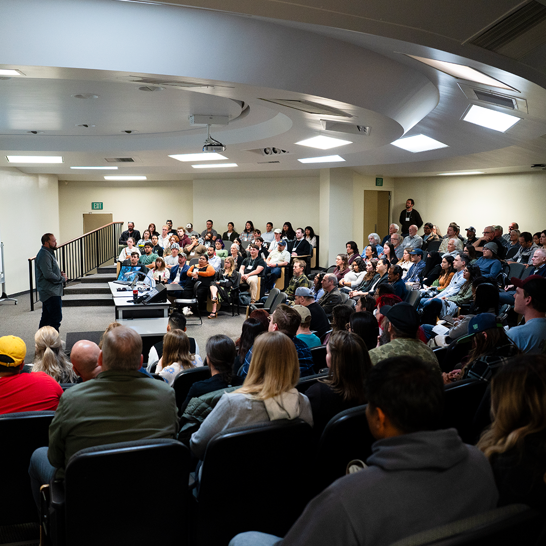 People seated in a large classroom listening to a speaker.