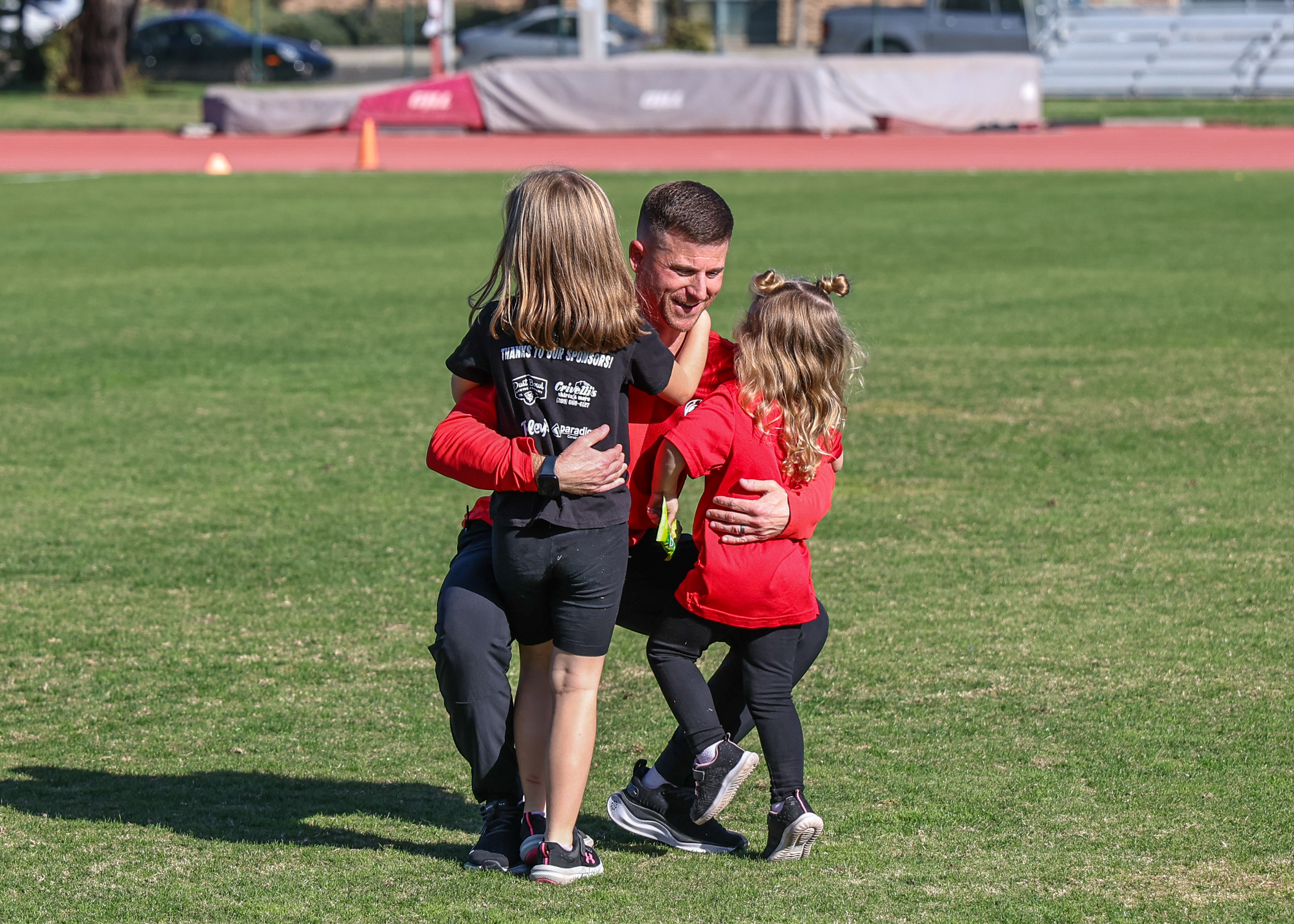 John Powell hugging his two daughters on the soccer field after a game.