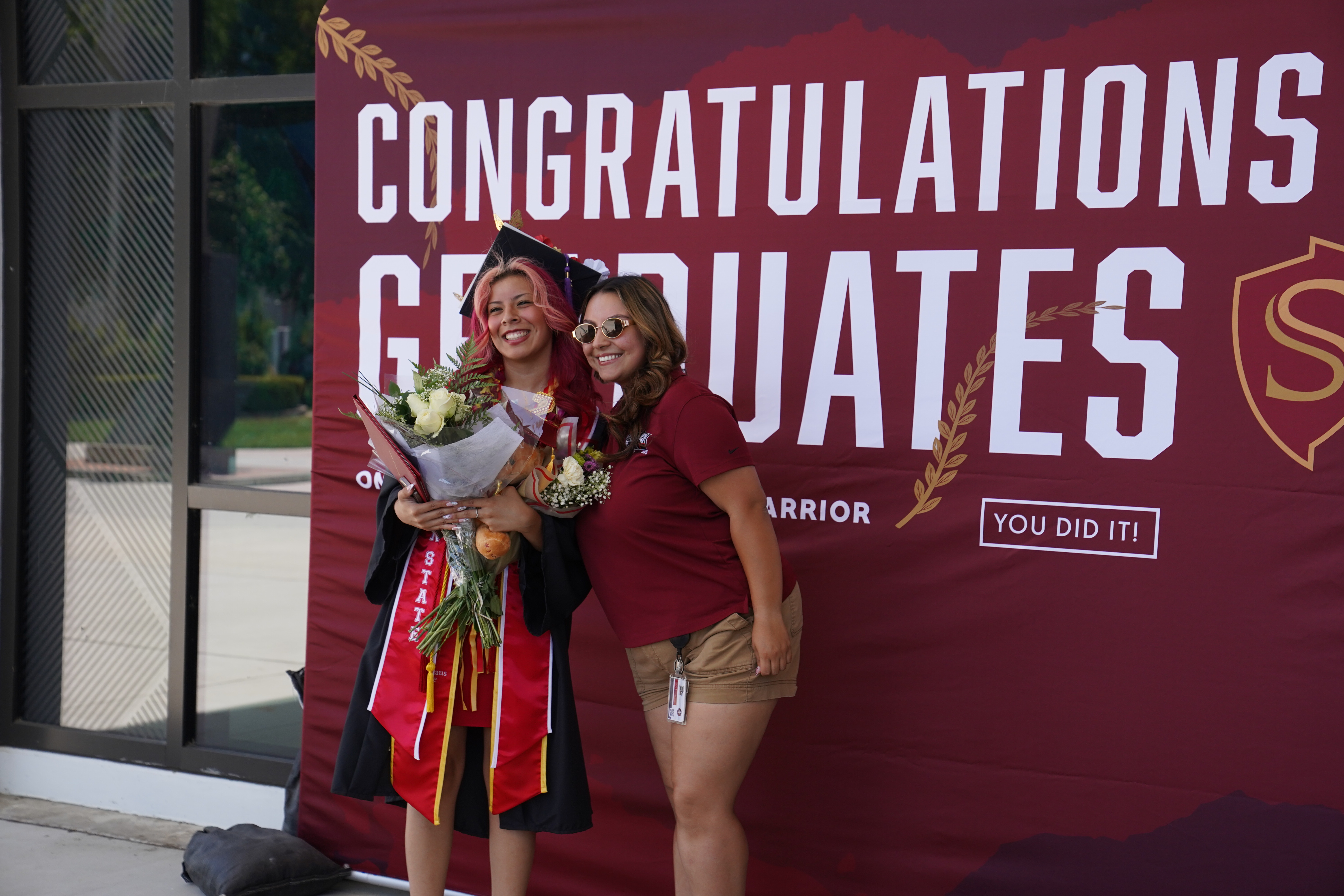 Graduating student and staff member posing in front of "congratulations graduates" sign