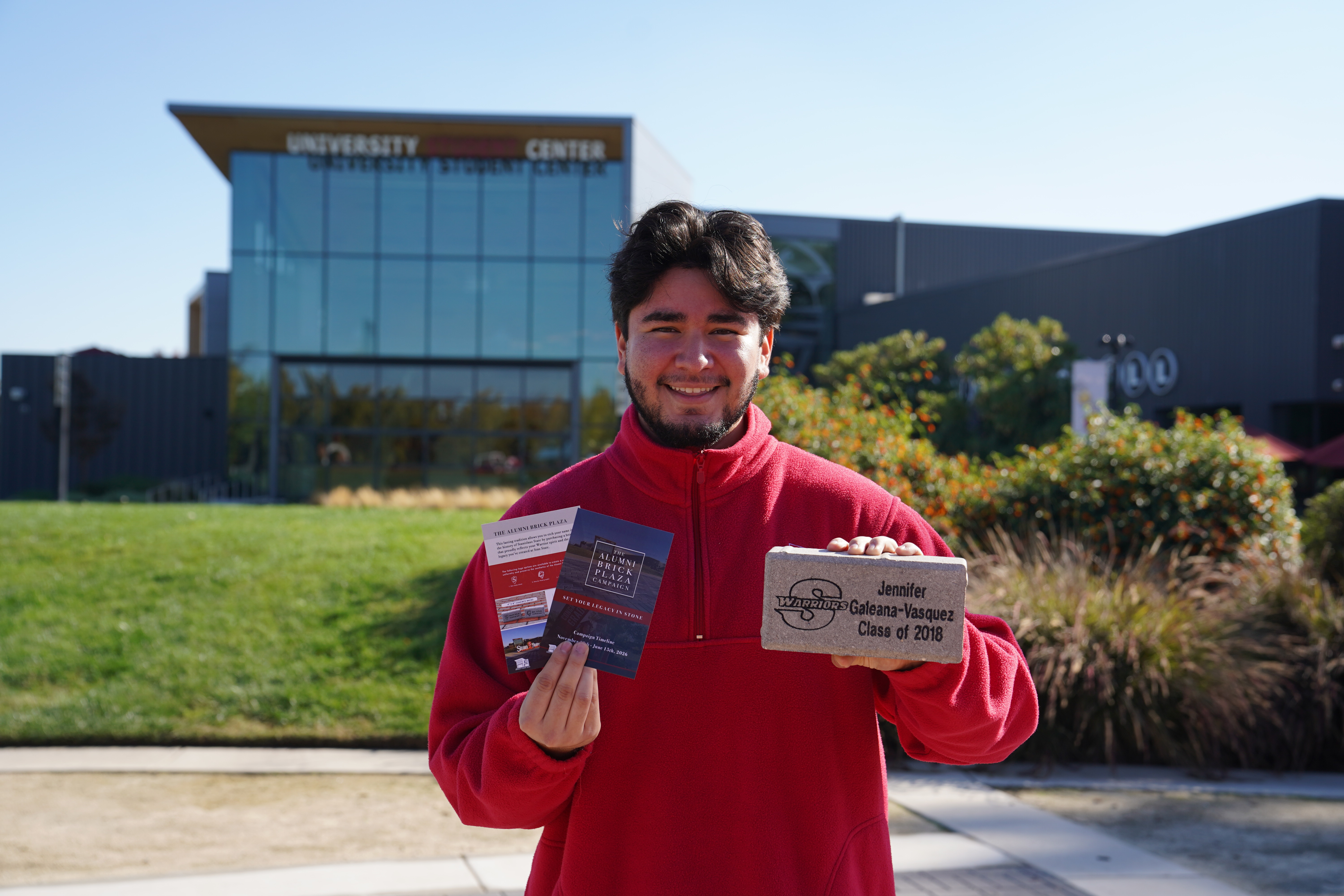 Student posing with alumni brick in front of student center