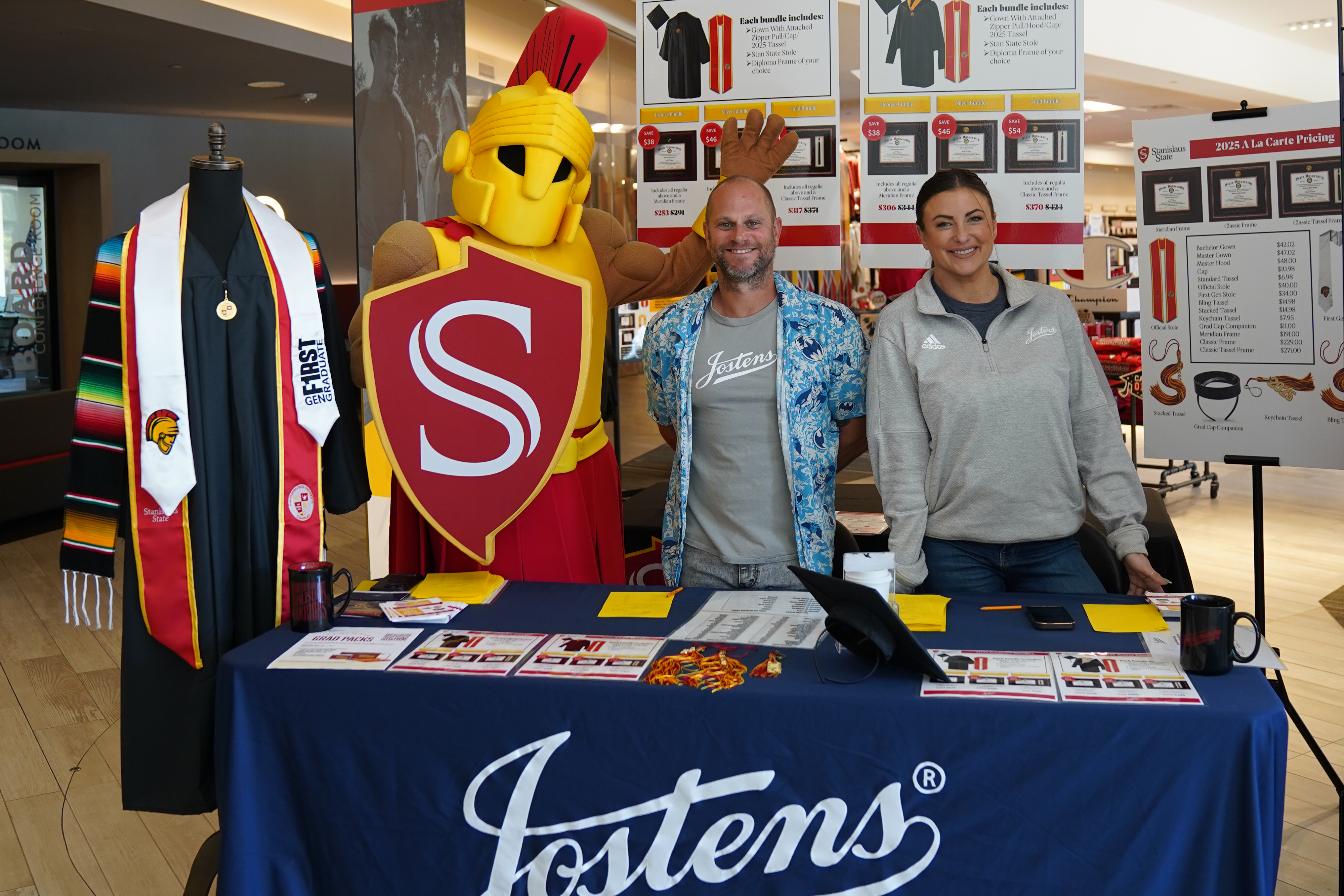 Titus posing with two individuals tabling for Jostens' Cap & Gown