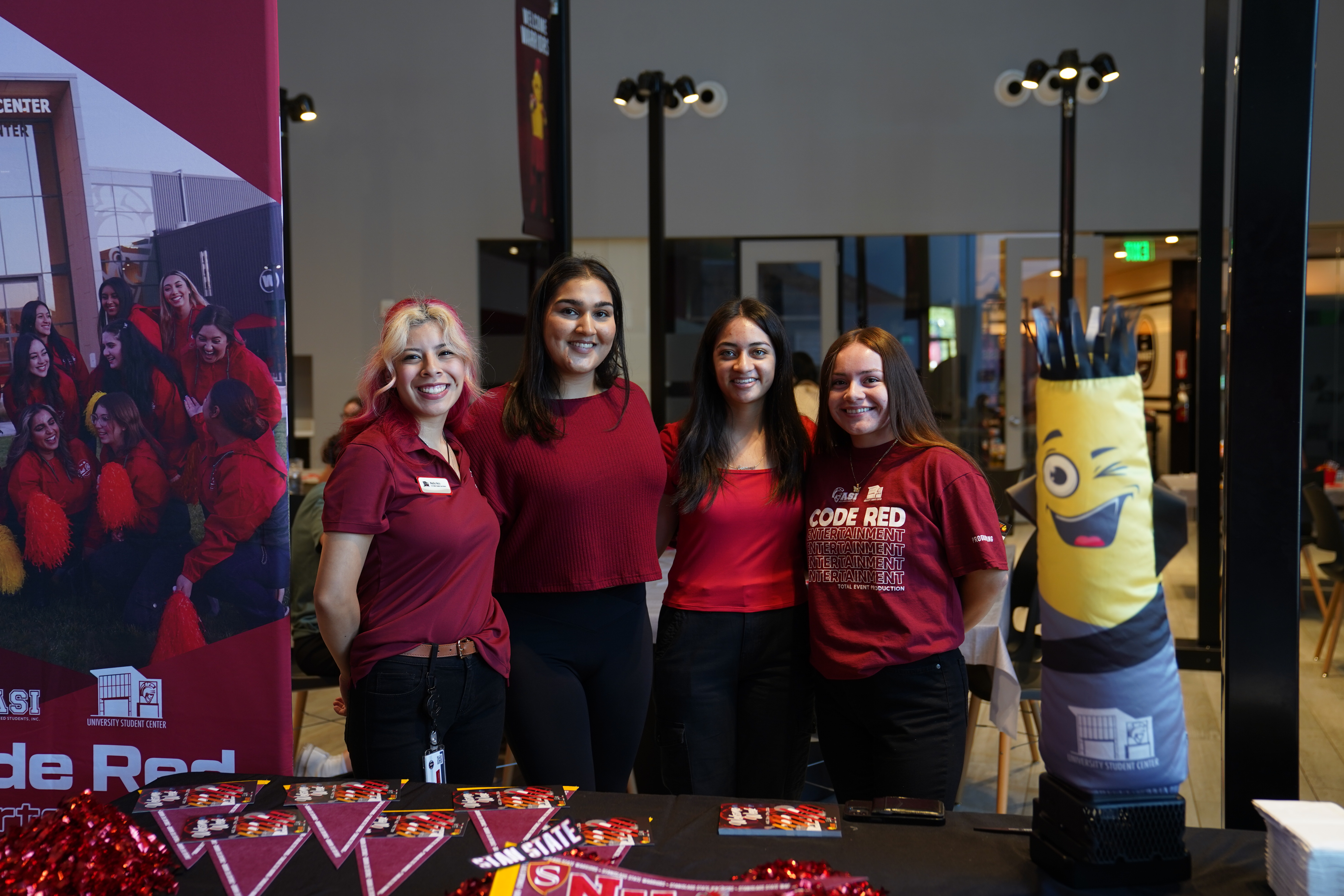 4 Students posed behind a promotion table inside the SC Lobby