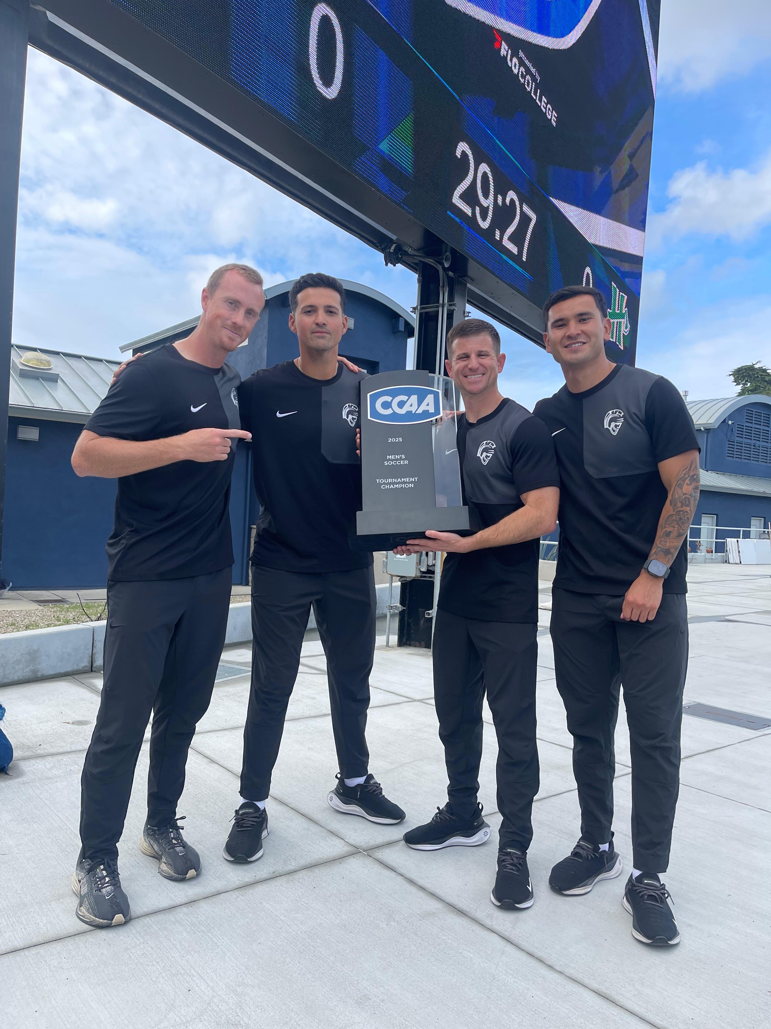 The Stan State Men's Soccer program coaching staff pose with the CCAA championship trophy.