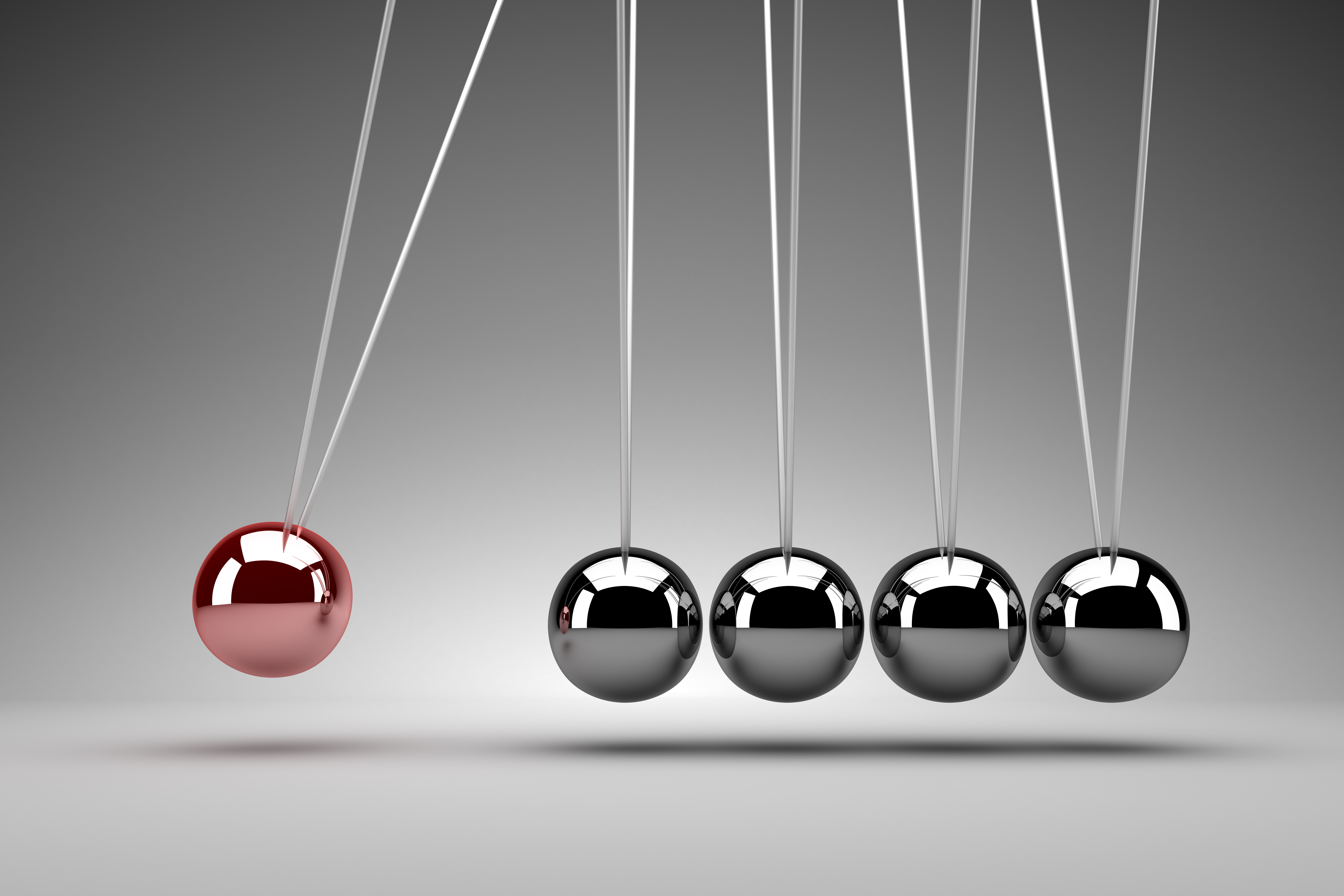 Newton’s cradle with one red ball pulled back and four silver balls aligned, illustrating motion and momentum.