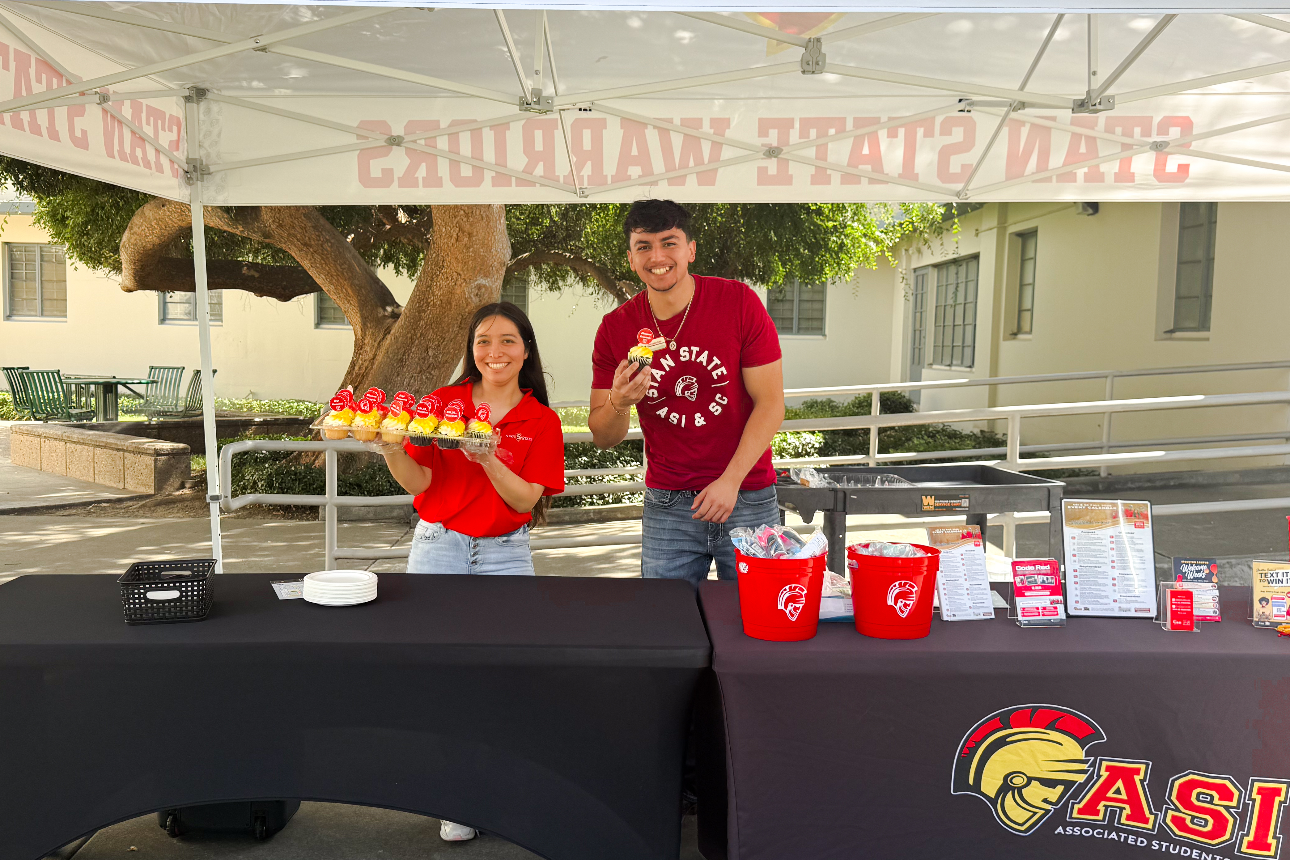 Two students holding cupcakes behind a table