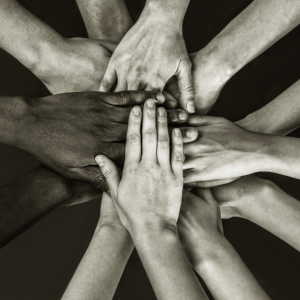 A group of people from different ethnic backgrounds places hands in the center of group
