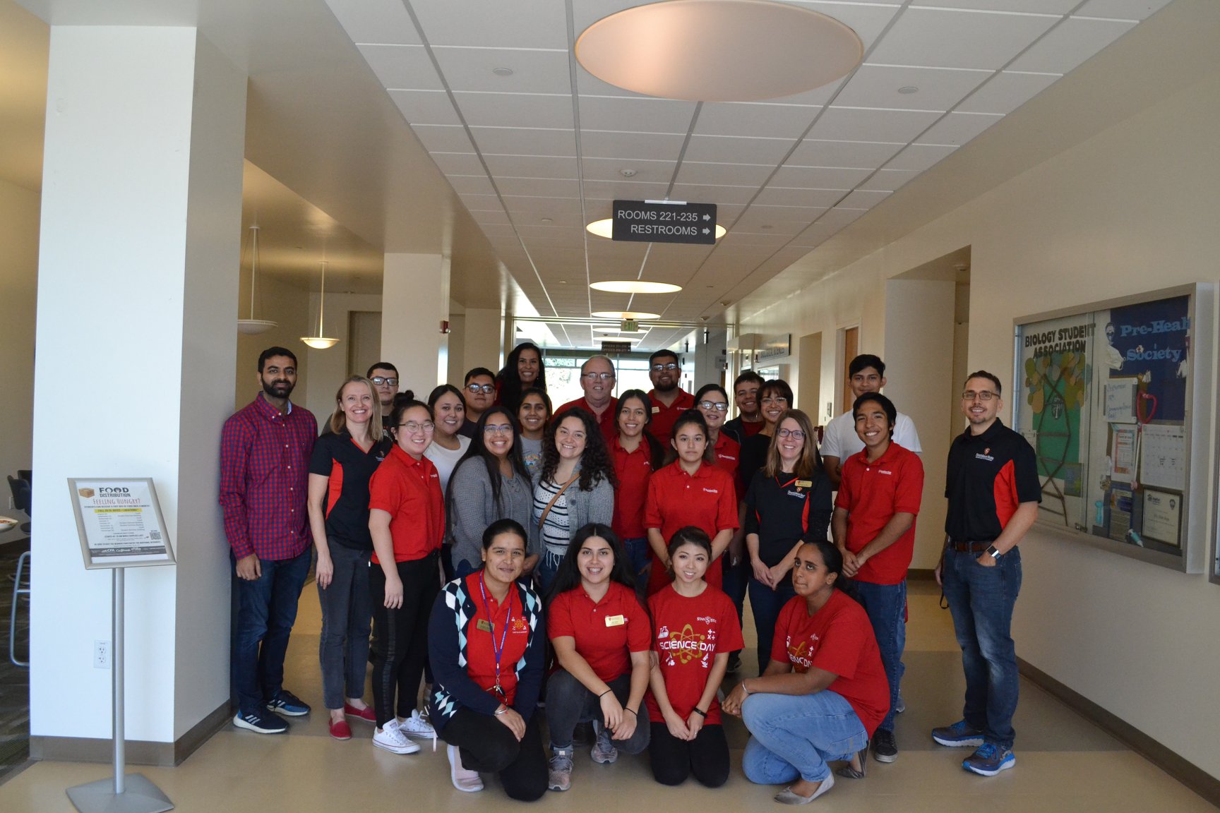 Group photo of students and staff in red shirts in a campus hallway.