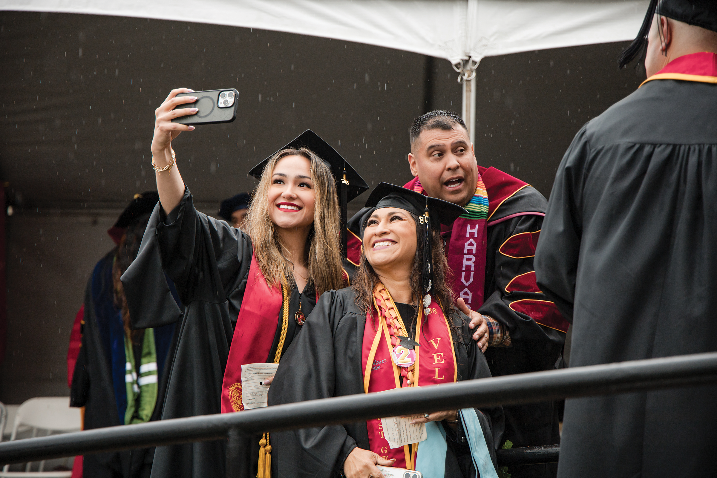 Graduates take a selfie in their regalia in the rain
