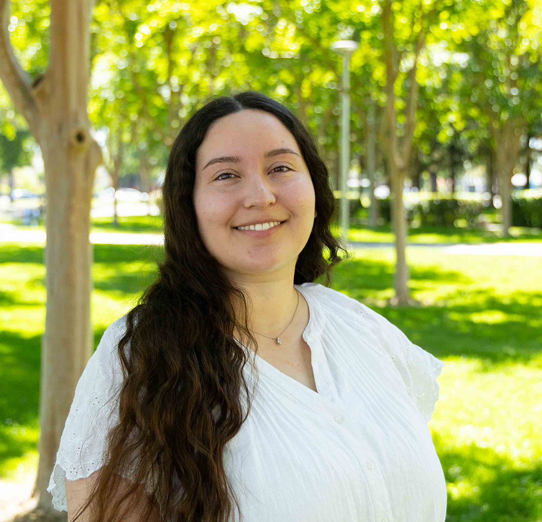 A woman in a white blouse and striped pants joyfully walks through a sunlit park, surrounded by trees and lush grass, exuding happiness and serenity.