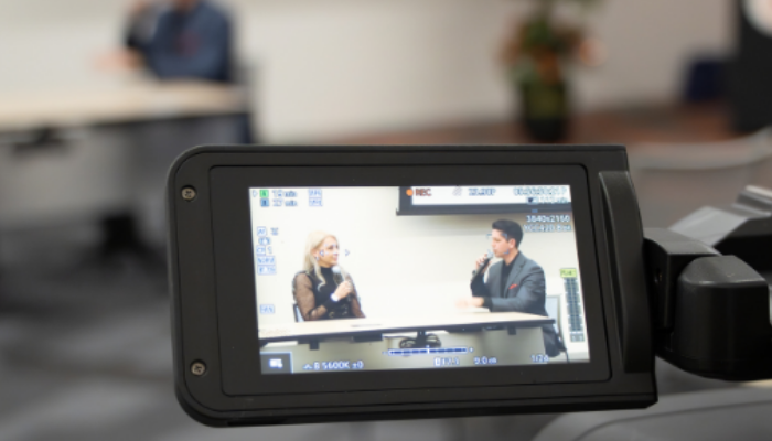 A handheld camcorder is seen filming a panel discussion