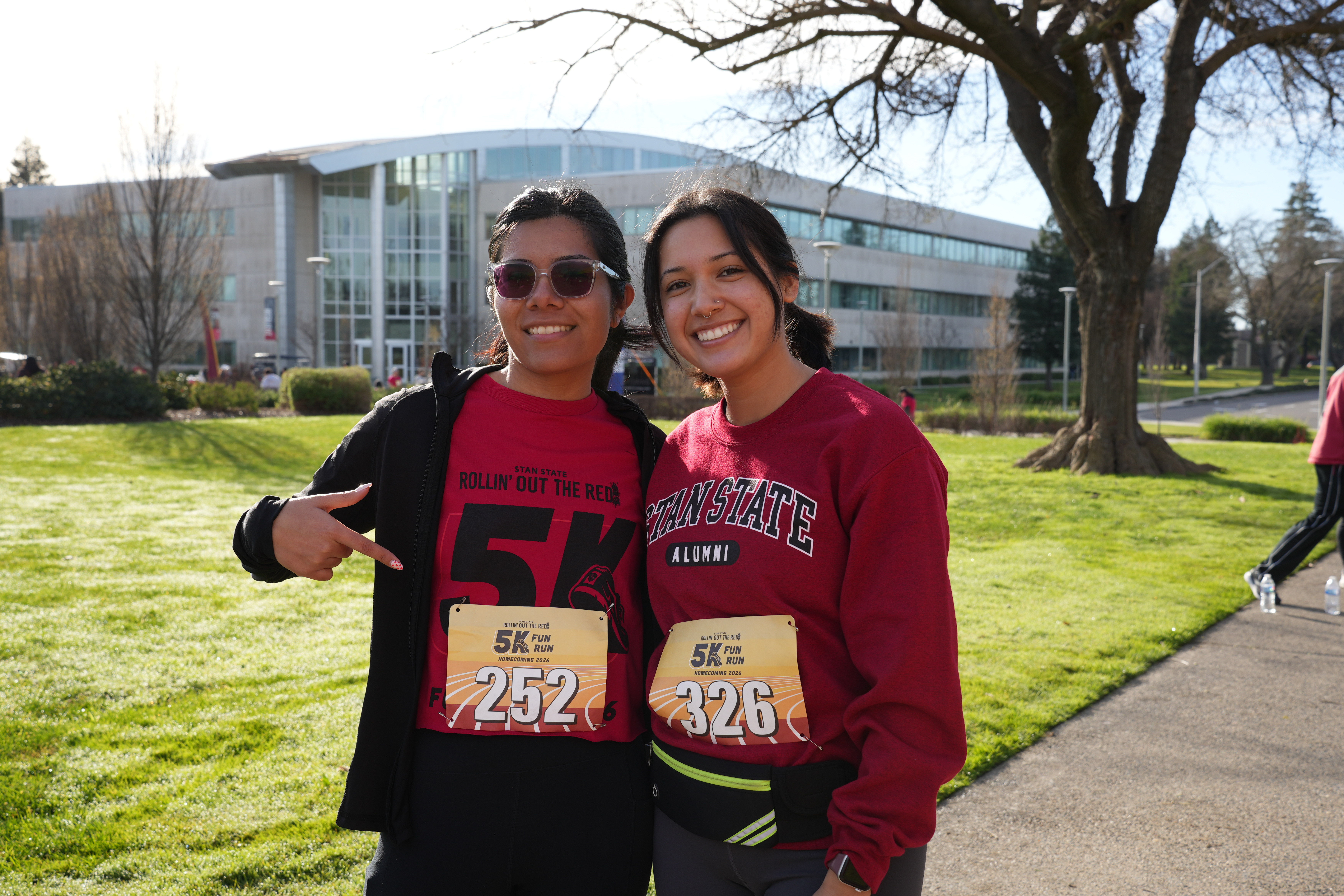 Two participants wear red shirts and race bibs while posing outdoors on campus during the Stan State 5K Fun Run.