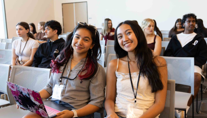 Two students smiling while seated in a campus presentation room. 