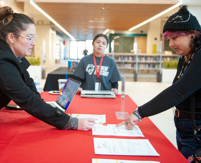 Student receiving assistance from staff at a campus services table.