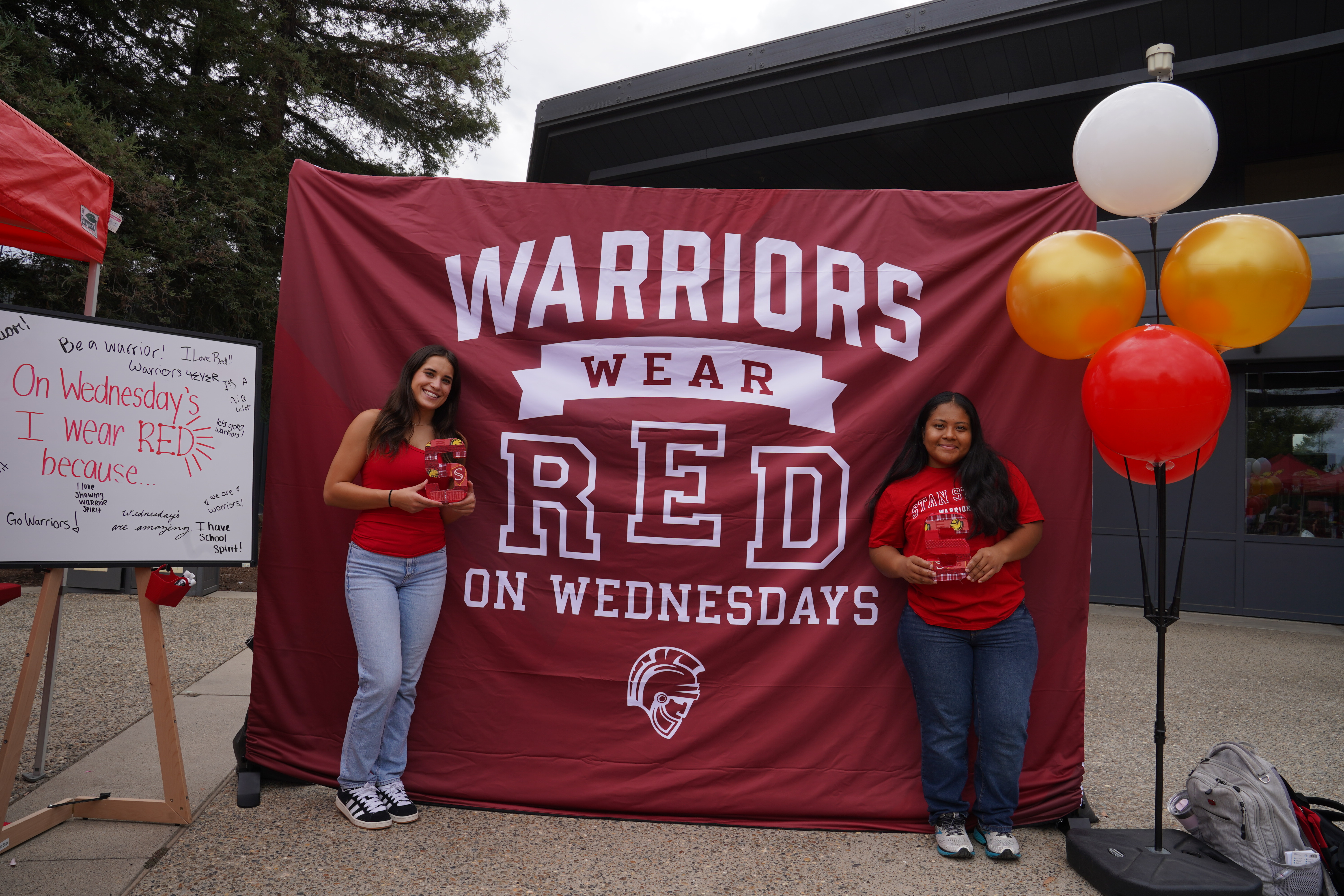 Students wearing red shirts in front of "Warriors Wear Red on Wednesdays" backdrop