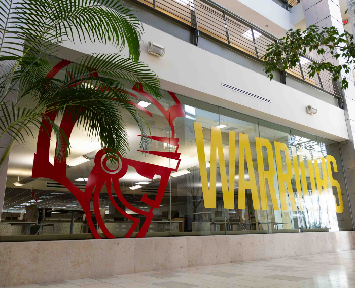 Interior view of the undergraduate advising area with a large Stan State Warrior graphic and yellow “WARRIORS” lettering on the glass wall.