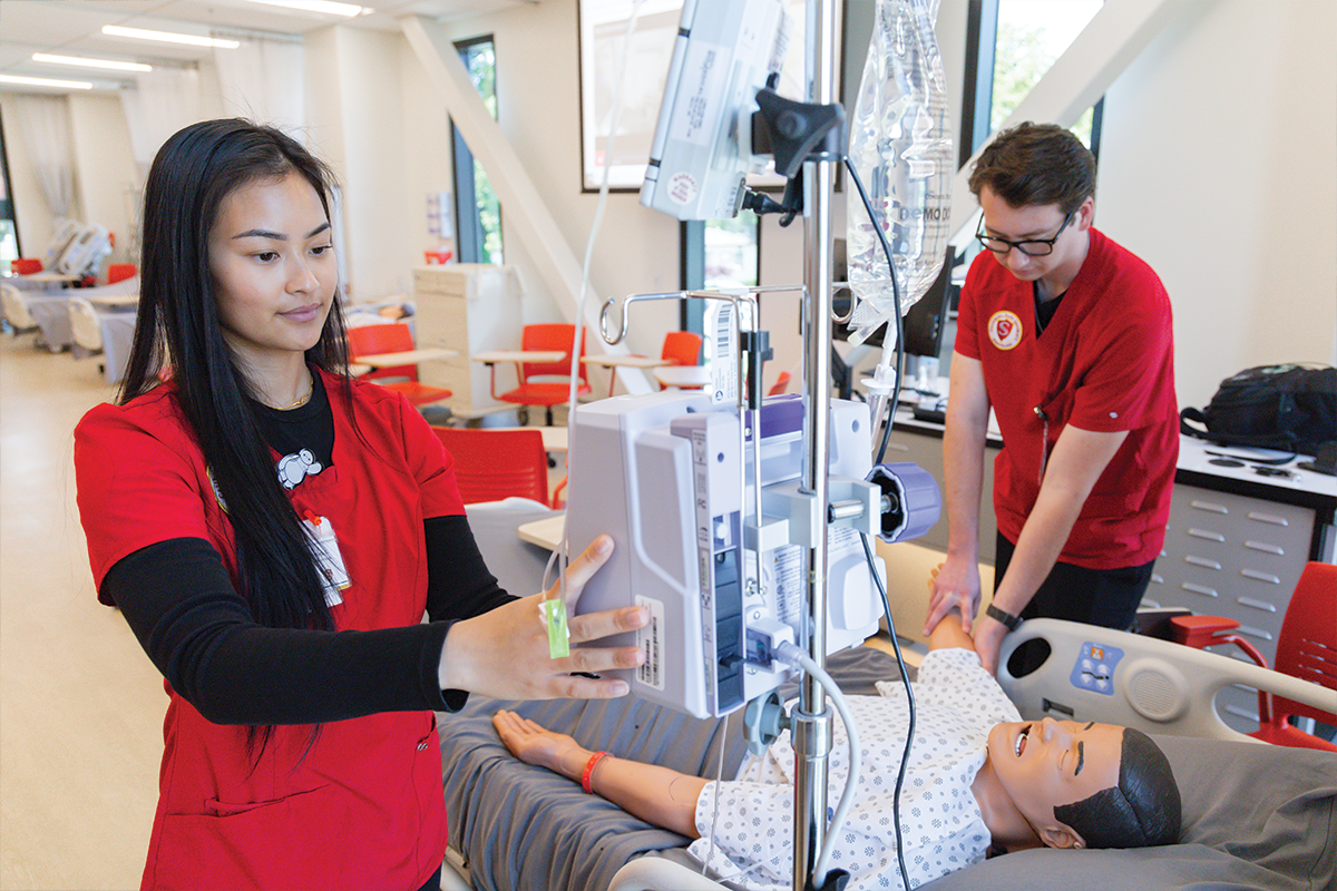 Two Stanislaus State nursing students practice patient care in a simulation lab.